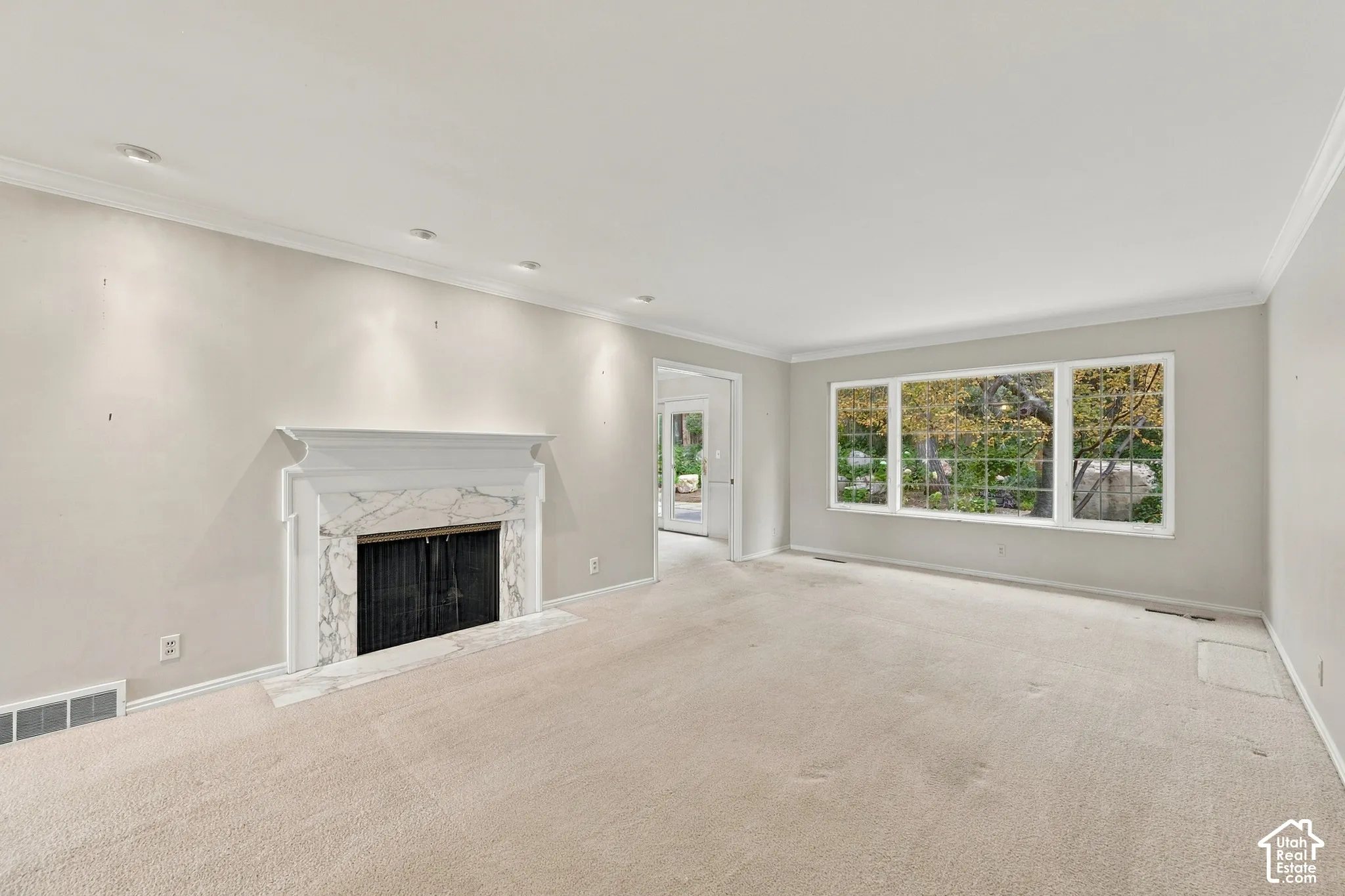Spacious room featuring a fireplace with a stone-surround mantel, expansive multi-pane windows, crown molding, and recessed lighting