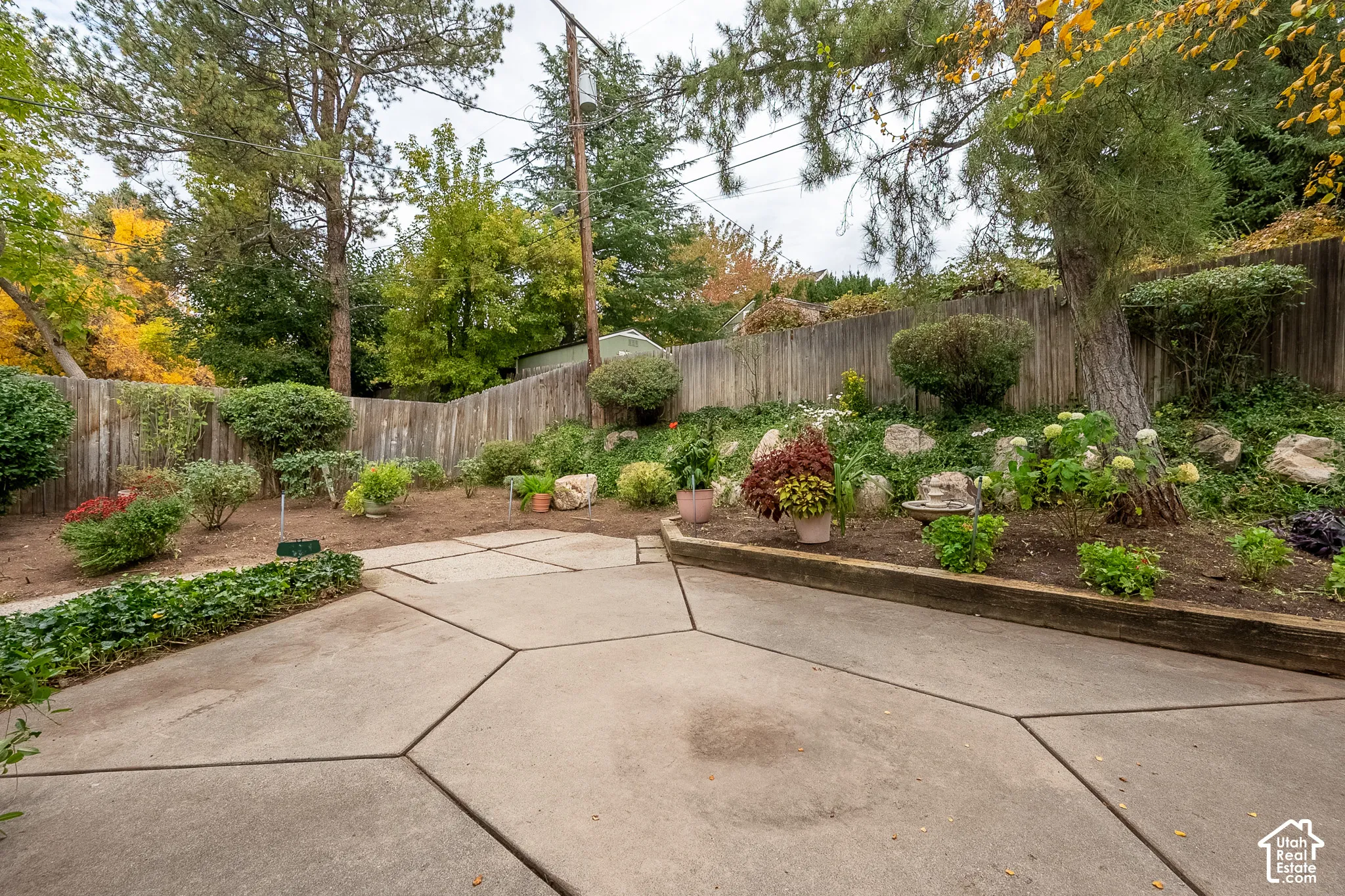 Concrete patio featuring geometric scoring, tiered landscaping, stone retaining walls, mature trees, and wooden perimeter fencing