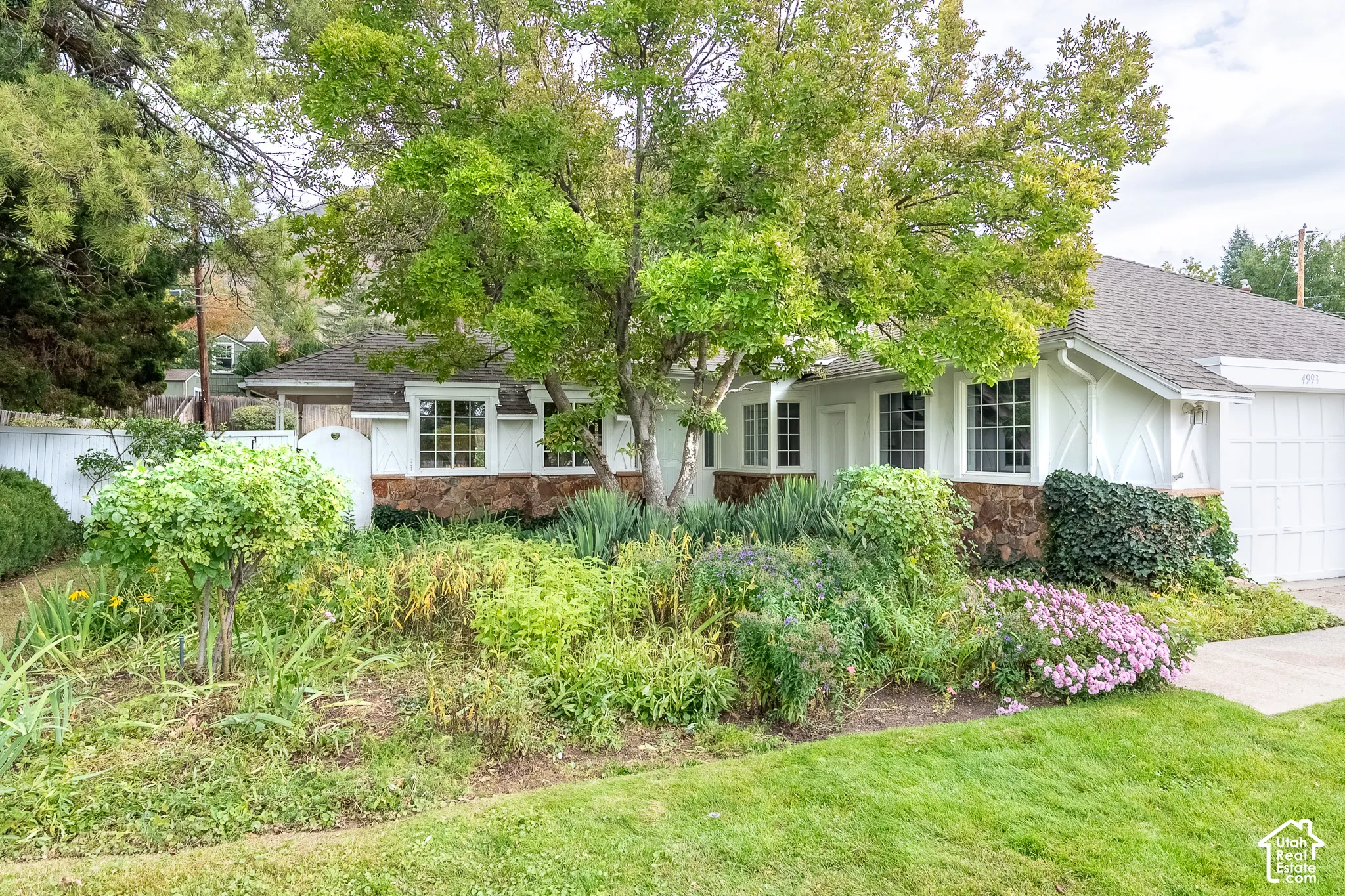 Exterior featuring stone masonry and white board-and-batten siding, multi-pane windows, and a mature tree-lined landscape