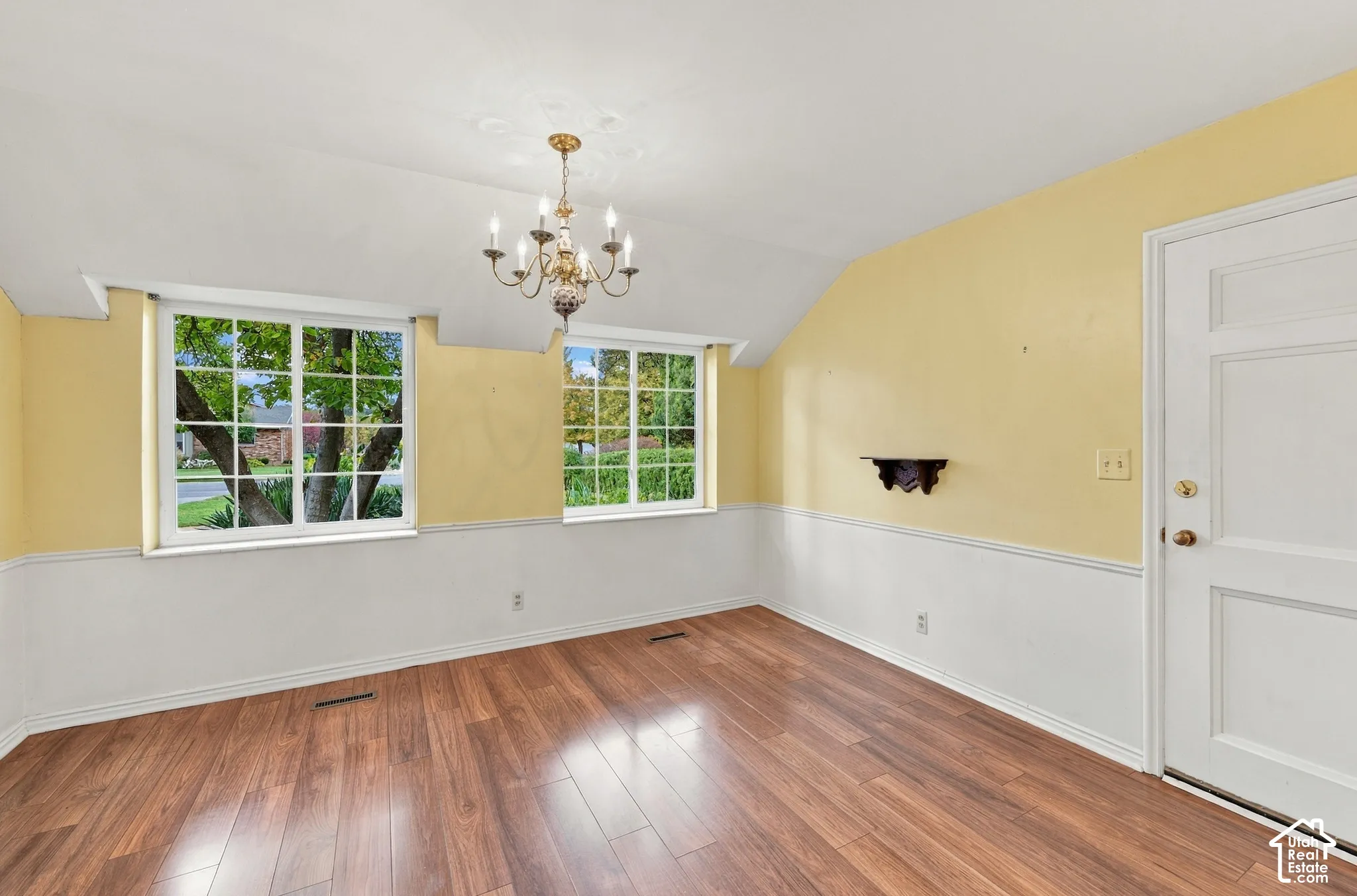 Room featuring wood-finish flooring, white wainscoting, dual multi-pane windows, and a multi-arm chandelier