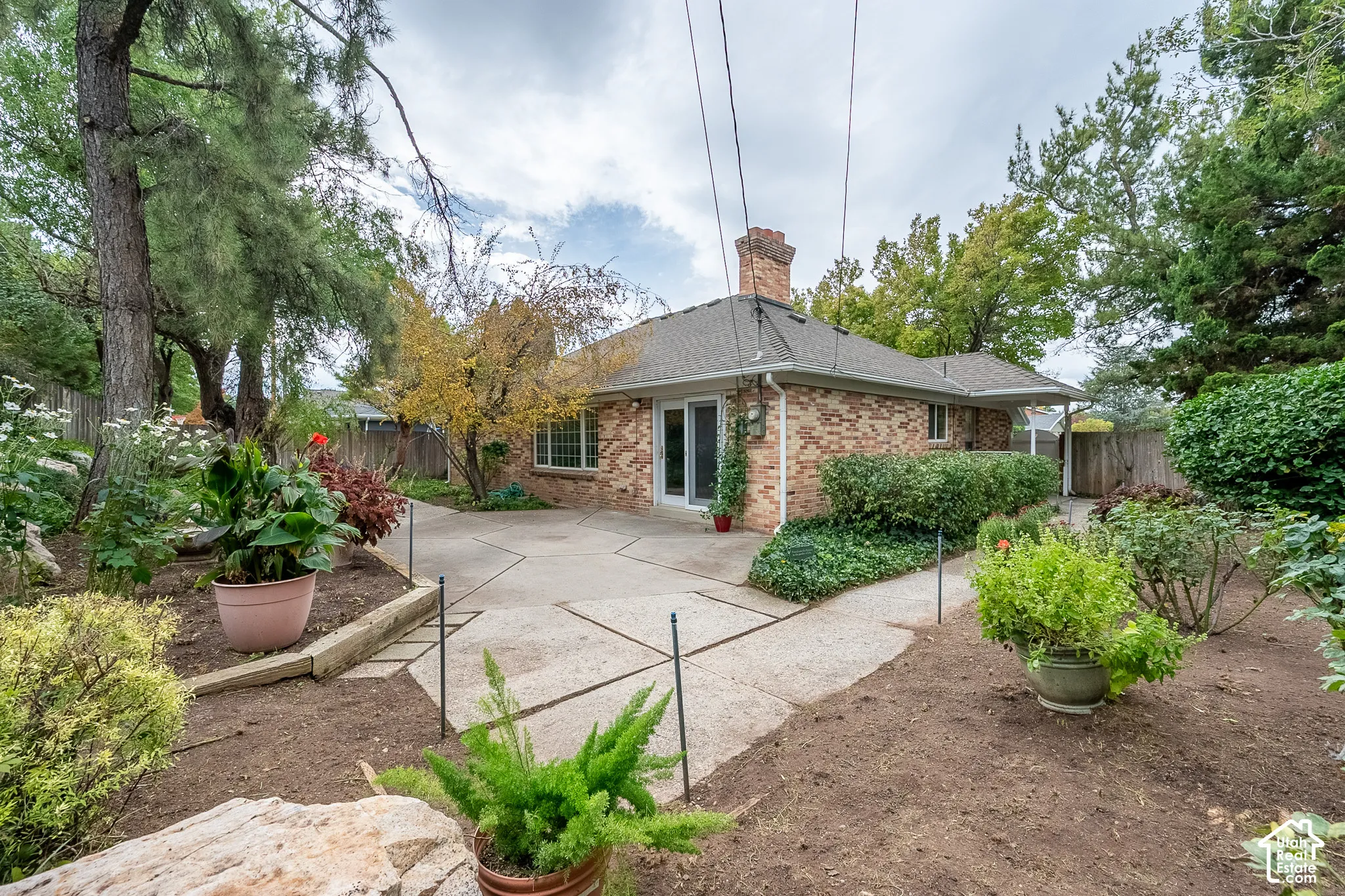 Exterior brick facade featuring a concrete patio, masonry chimney, and wood-retained landscaping beds