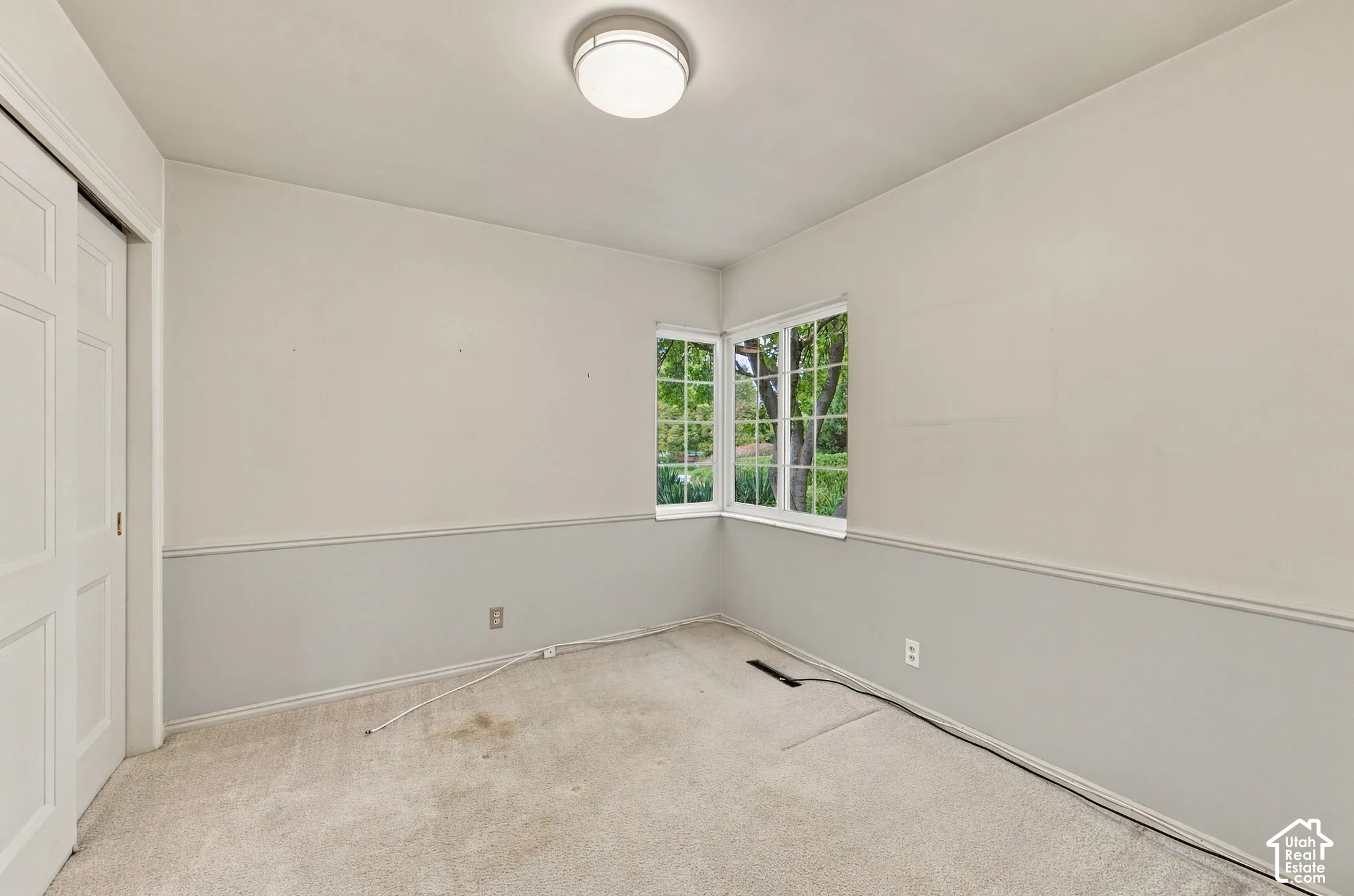 Bedroom 1 featuring neutral carpeting, two-toned wall paint with chair rail molding, a flush-mount ceiling light fixture, and a multi-pane corner window