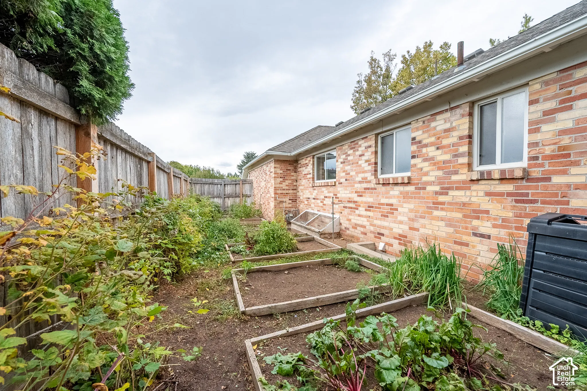 Brick exterior with multiple raised garden beds, wood-slat privacy fencing