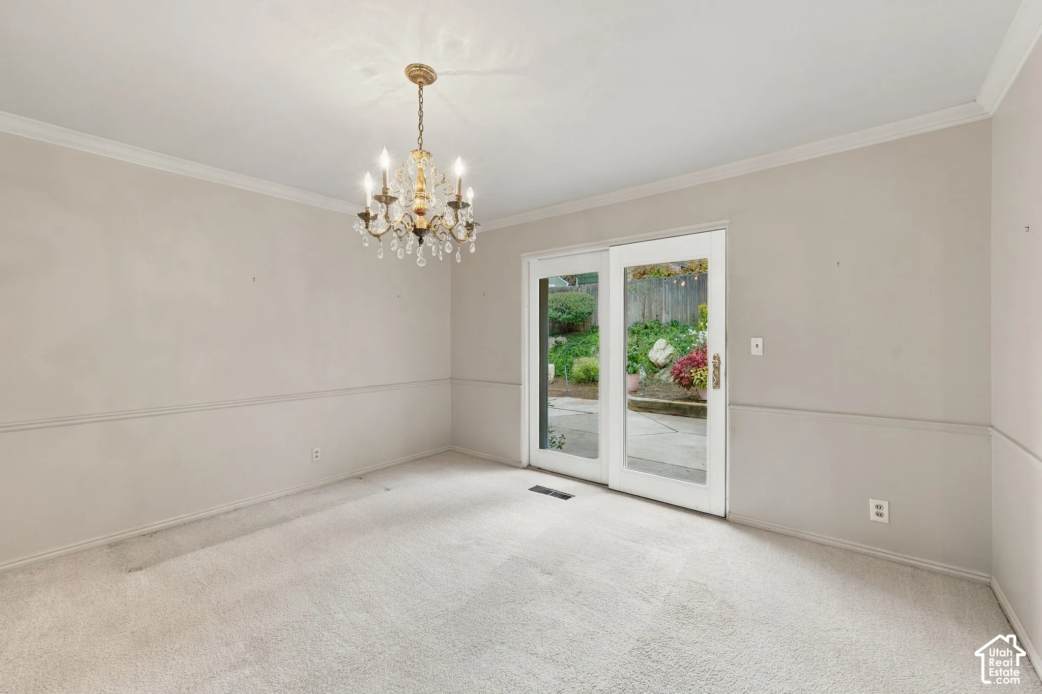 Dining room  featuring crown molding, chair rail trim, a multi-light crystal chandelier, and glass-paned sliding doors opening to an outdoor patio