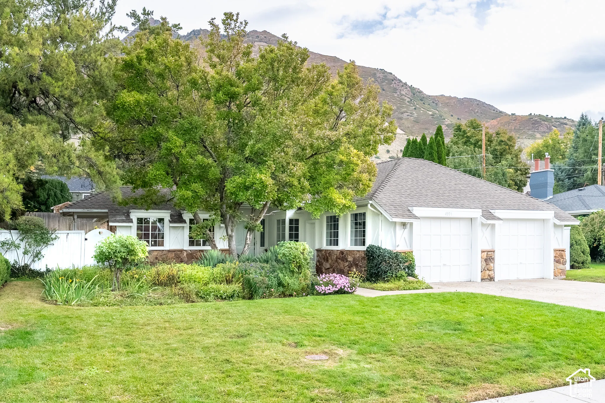 Picturesque residence featuring natural stone exterior accents, a white-panel garage, multi-pane windows, and a mountain backdrop