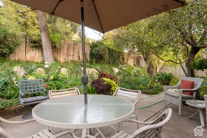 Patio area featuring concrete surfacing, a privacy fence, established trees, and varied landscaping