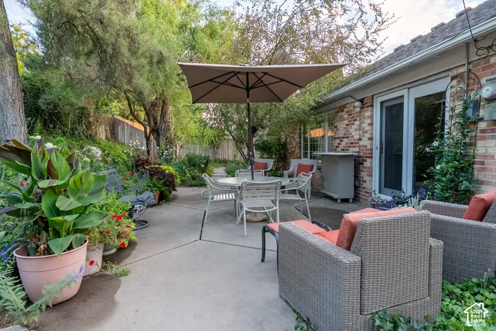 Concrete patio with surrounding garden beds, mature trees, and a brick exterior