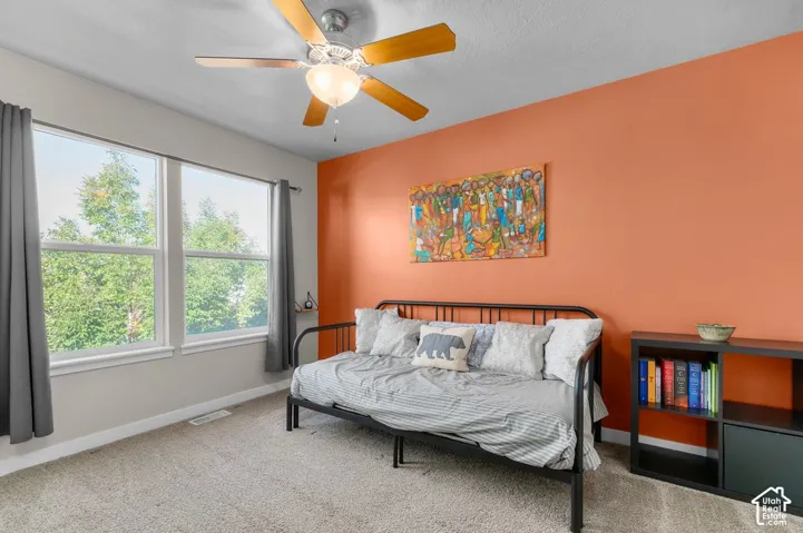 Carpeted flooring, a ceiling fan with integrated lighting, and multiple windows providing natural illumination