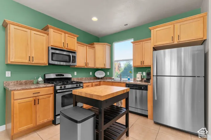 Kitchen featuring wood-finish cabinetry, stainless steel appliances, a center island with a butcher block top, and a window above the sink