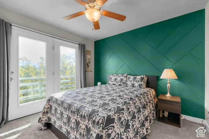 Dual French doors leading to an outdoor balcony, accent wall with geometric paneling, ceiling fan with integrated lighting, and carpeted flooring