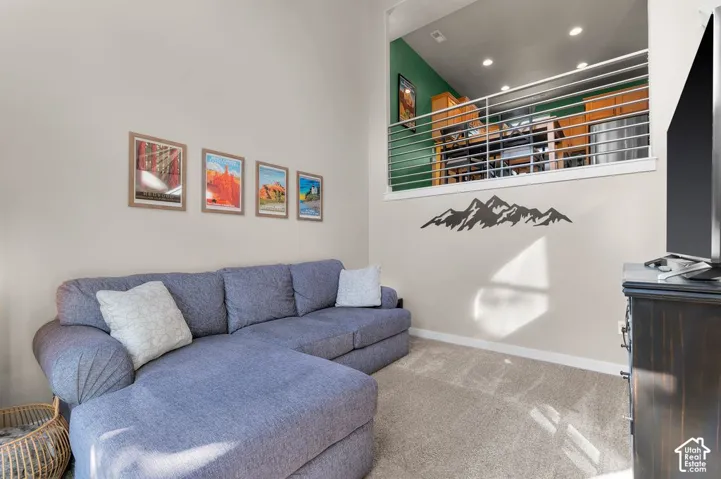 Loft space with metal railing overlooking a room with carpeted flooring