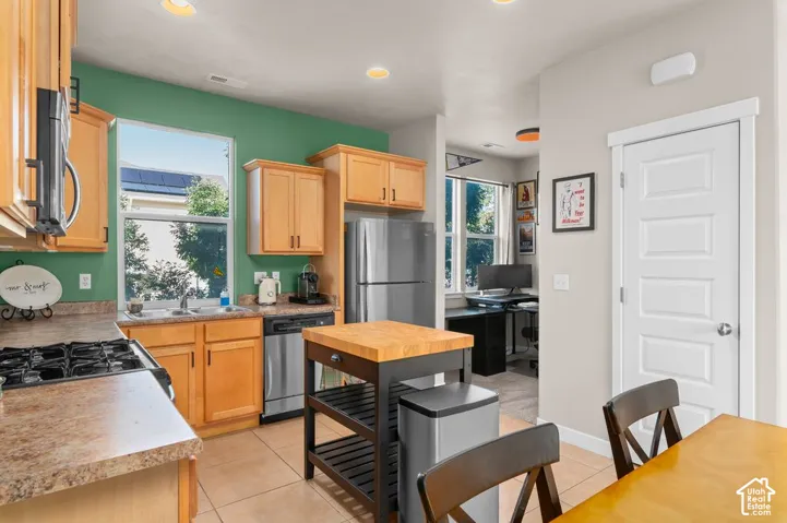 Kitchen featuring light wood cabinetry, a stainless steel refrigerator, a stainless steel dishwasher, a gas range, and a kitchen island with a butcher block top