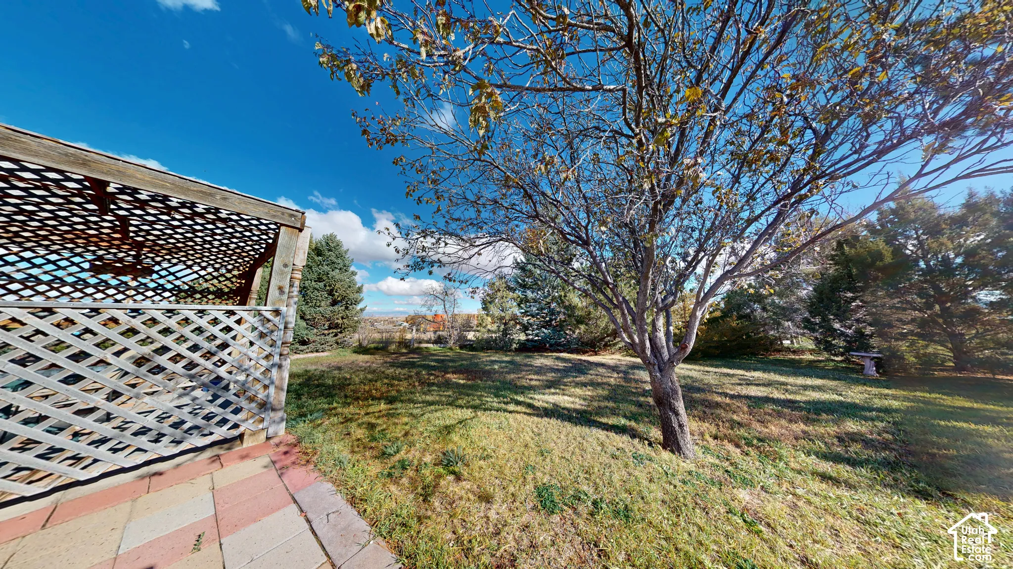 Outdoor space featuring a latticed pergola, paved patio, mature trees, and expansive lawn area