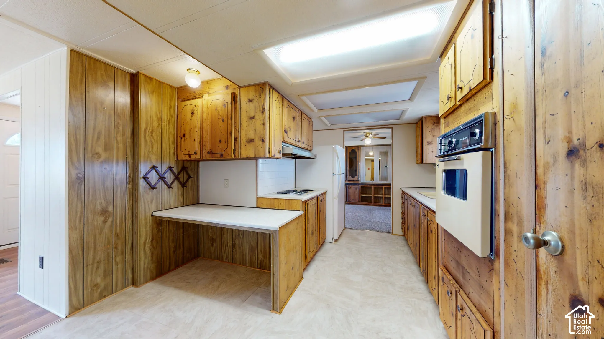 Kitchen featuring wood cabinetry, built-in wall oven, inset stovetop, and fixed laminate countertop