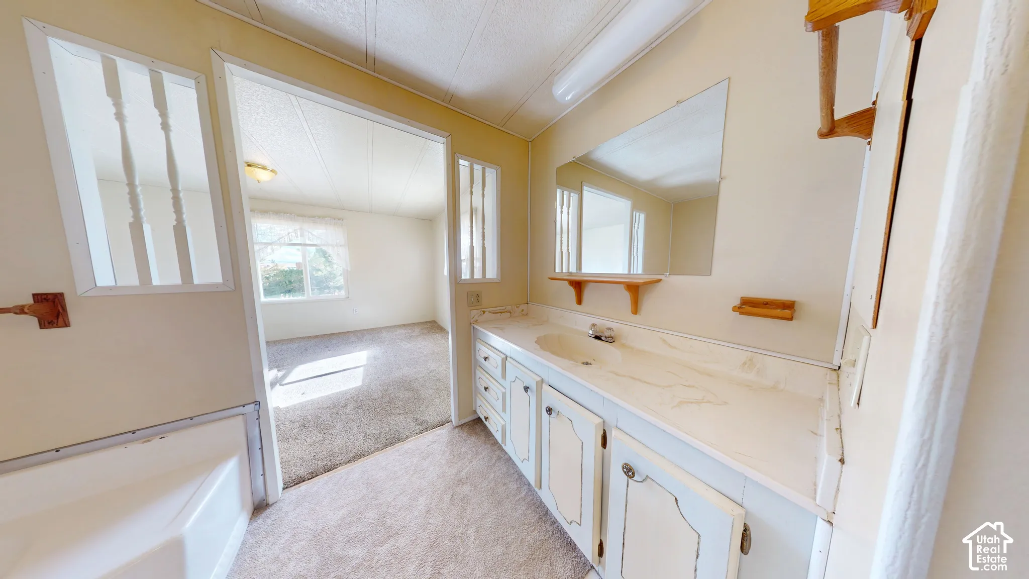 Bathroom featuring a vanity with integrated sink and countertop, wall-mounted mirror, wood-finish shelving, and decorative spindle accents
