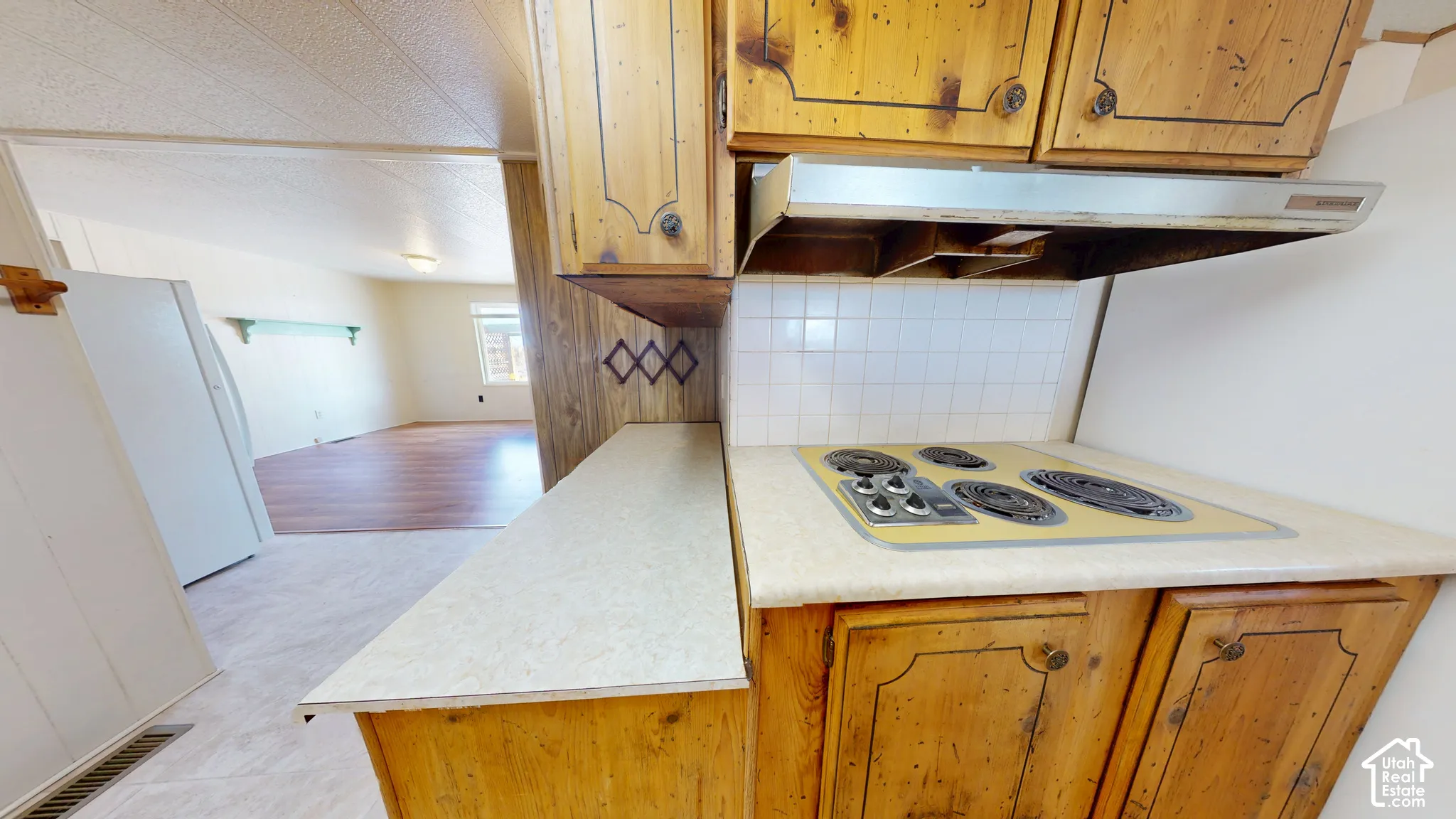 Kitchen featuring wood cabinetry, integrated electric cooktop, stainless steel range hood, square tile backsplash, and light-toned laminate countertops