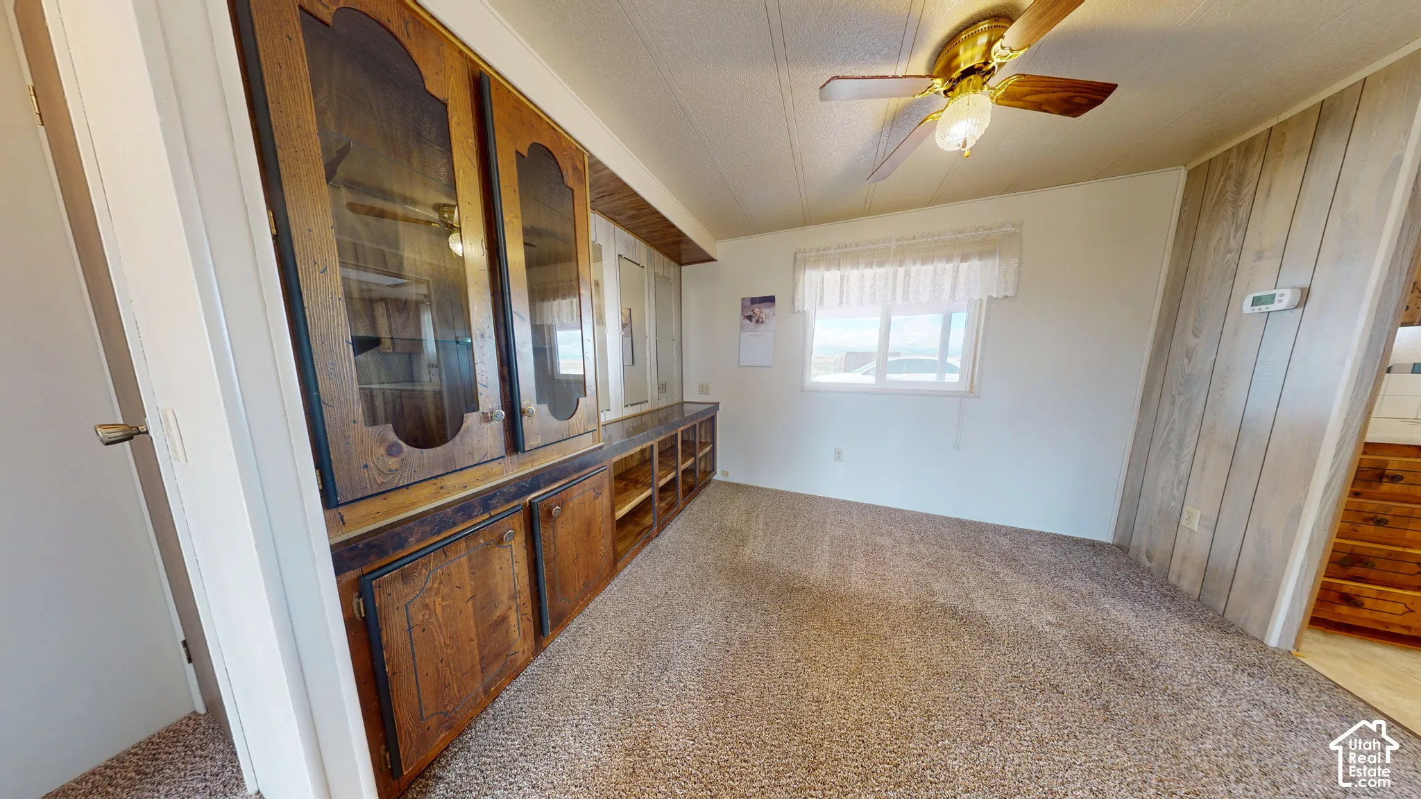 Built-in wooden cabinetry with glass-panel display doors, wall-mounted wood-finish paneling, and a ceiling fan with integrated lighting