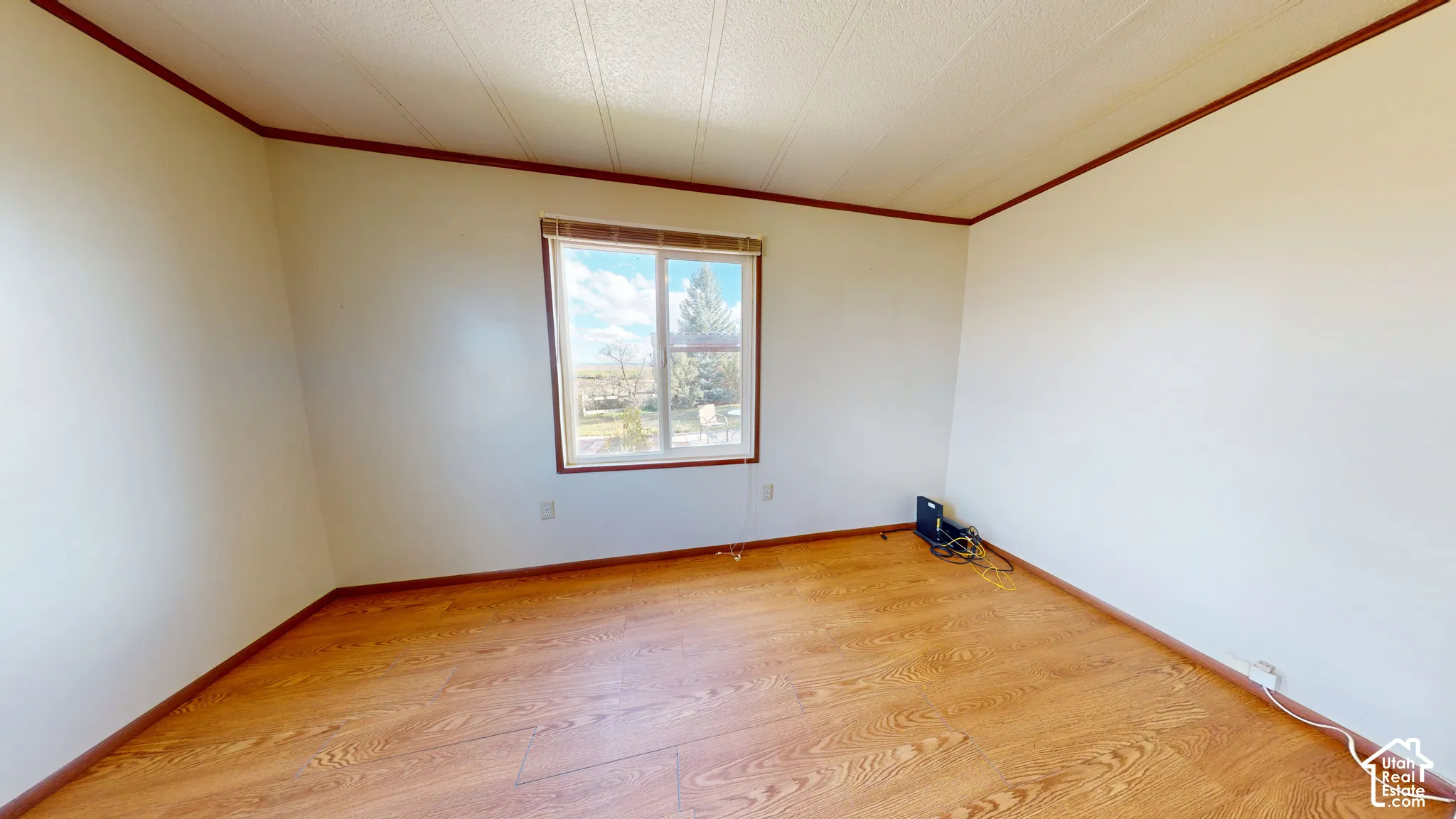 Room featuring wood-finish flooring, a single-pane sliding window, and neutral wall tones accented by wood-finish trim