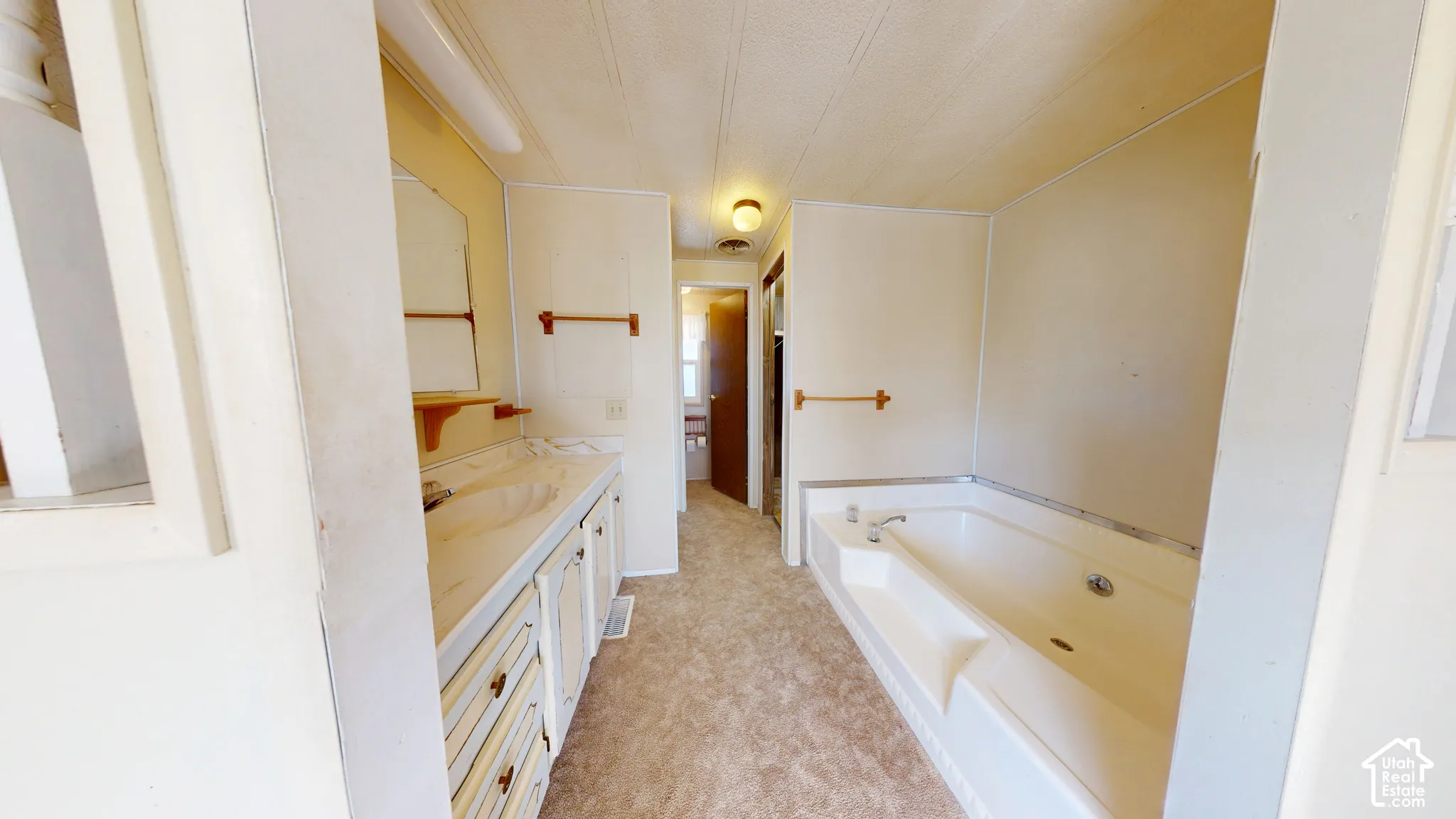 Bathroom featuring a built-in soaking tub, vanity with integrated sink, wood-finish cabinetry, and wall-mounted fixtures