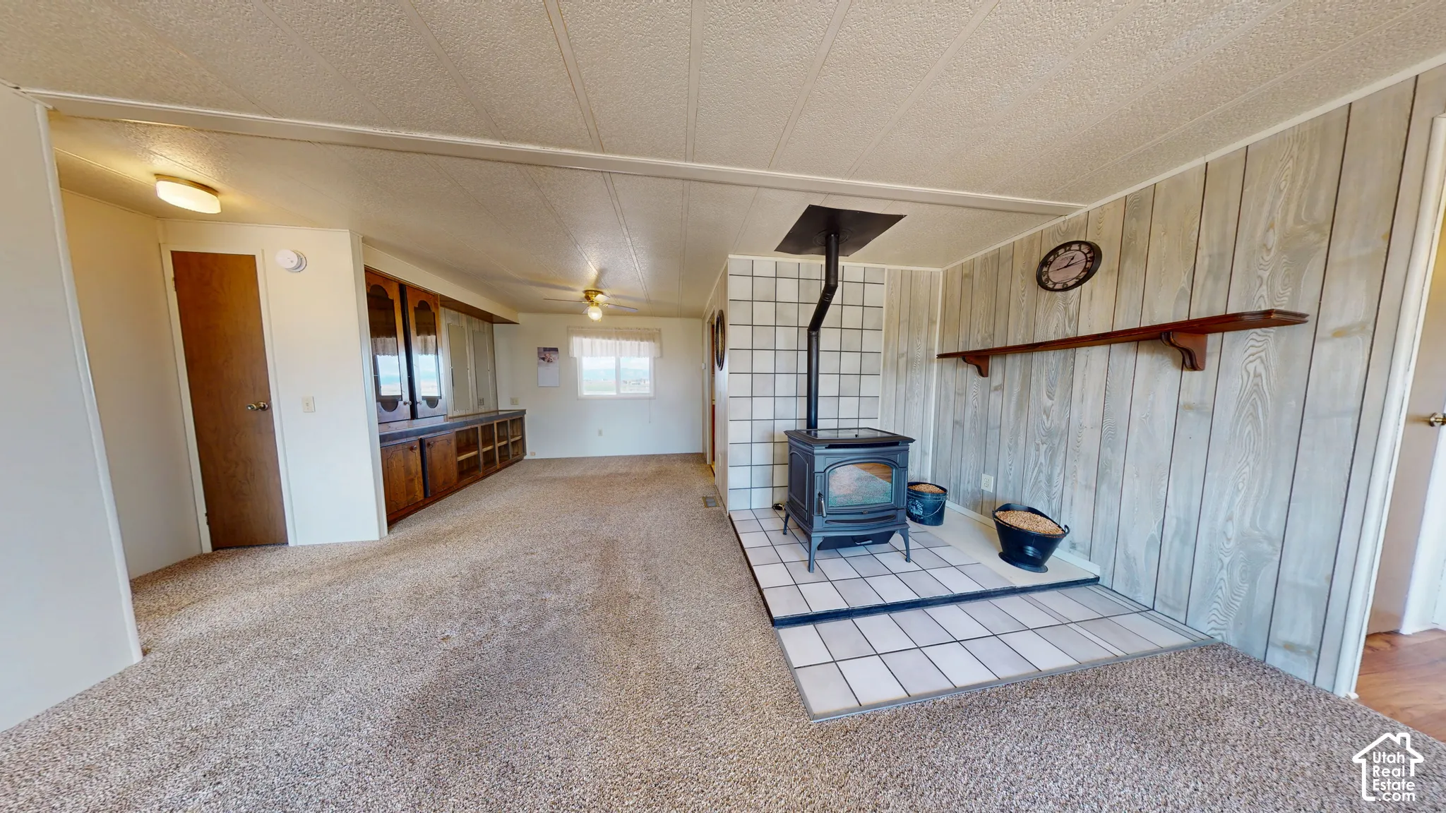 Living area featuring a freestanding cast-iron stove, tiled hearth, wood-paneled wall with fixed shelving, and built-in cabinetry