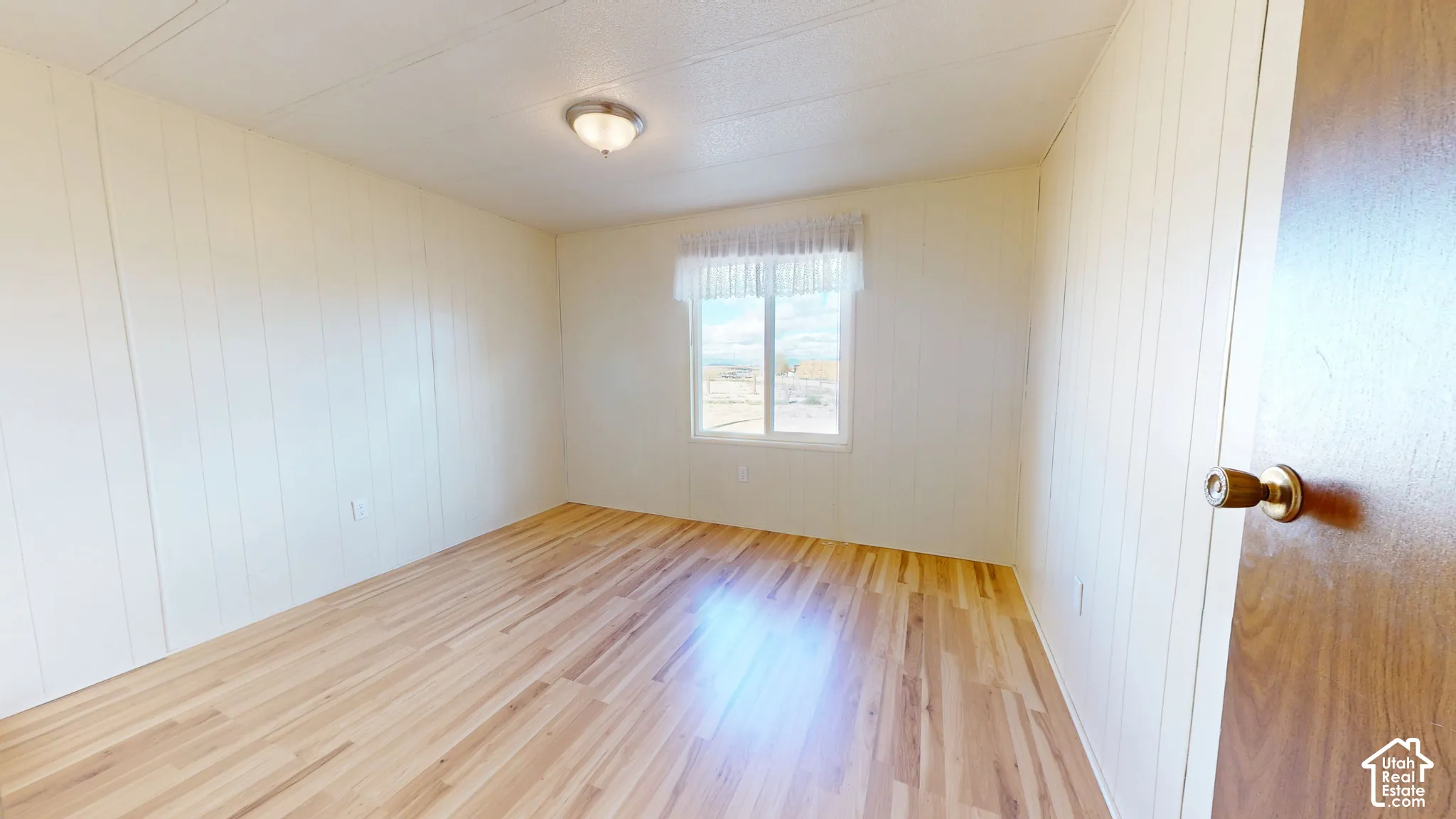 Room featuring wood-finish flooring, vertical-panel walls, and a single-pane sliding window