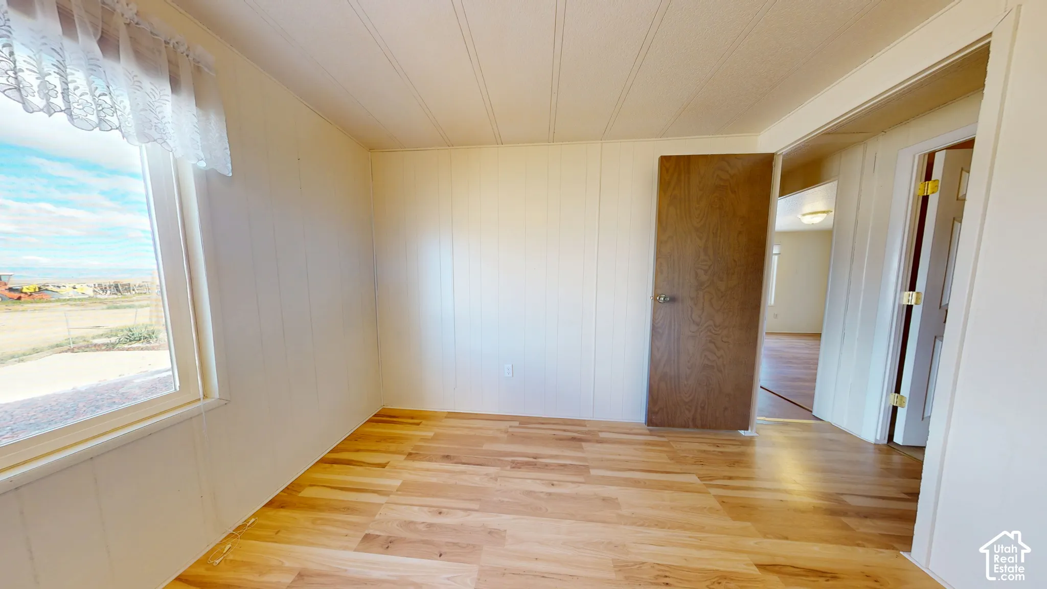 Interior room featuring wood-finish flooring, white panel walls, and a large window