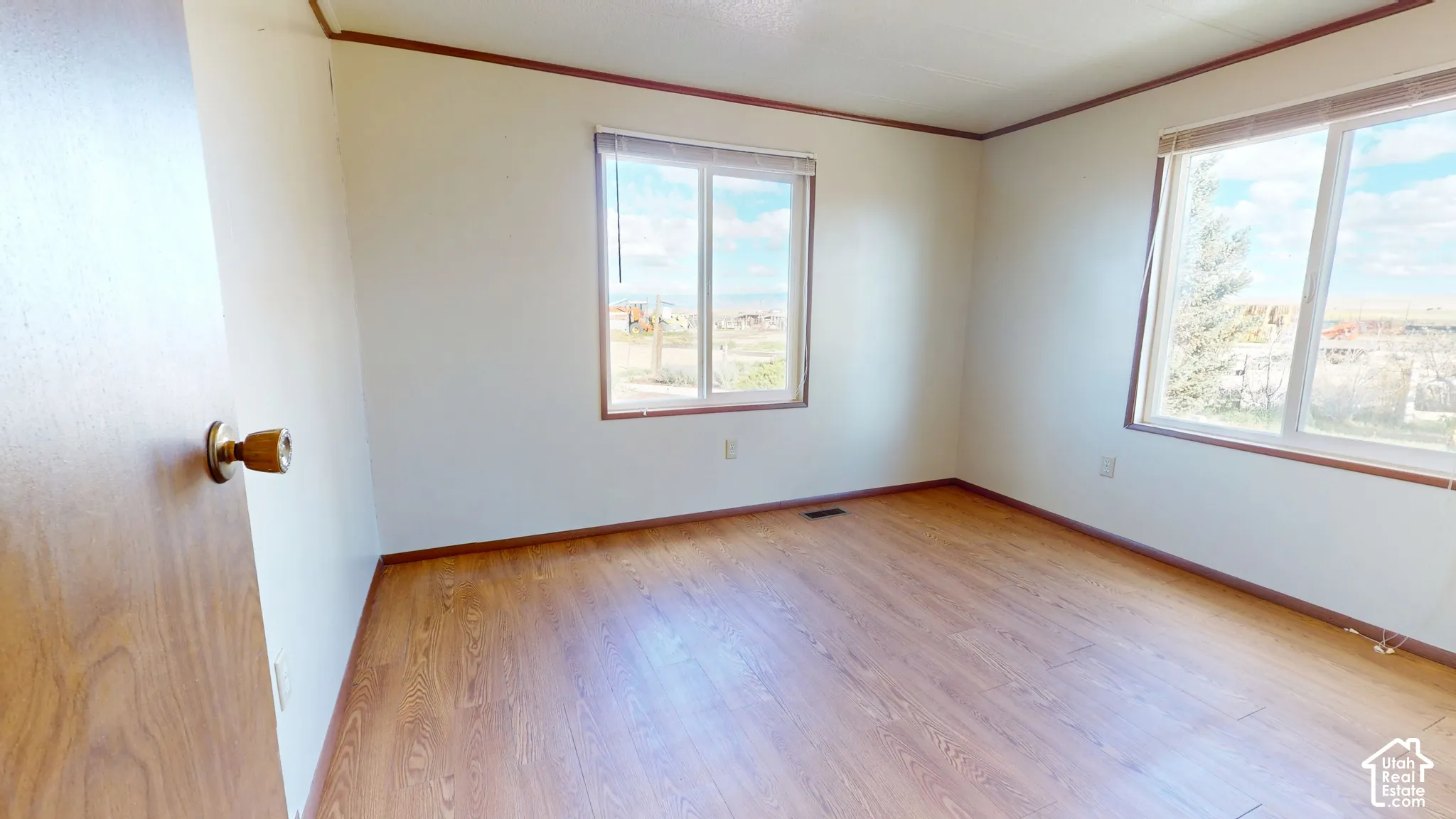 Room featuring wood-finish flooring, dual windows with horizontal blinds, and solid-core door with metallic hardware