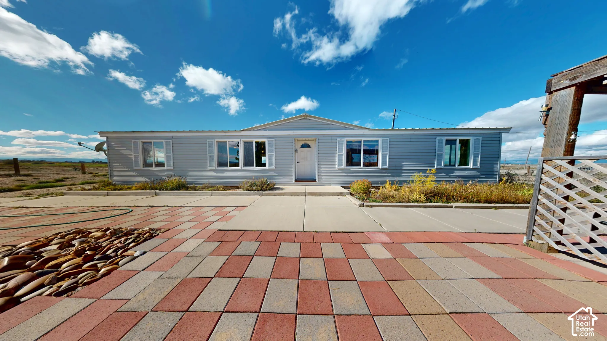 Single-story residence featuring light gray siding, a paved patio with multi-tonal brick pavers, window shutters, and a covered lattice structure