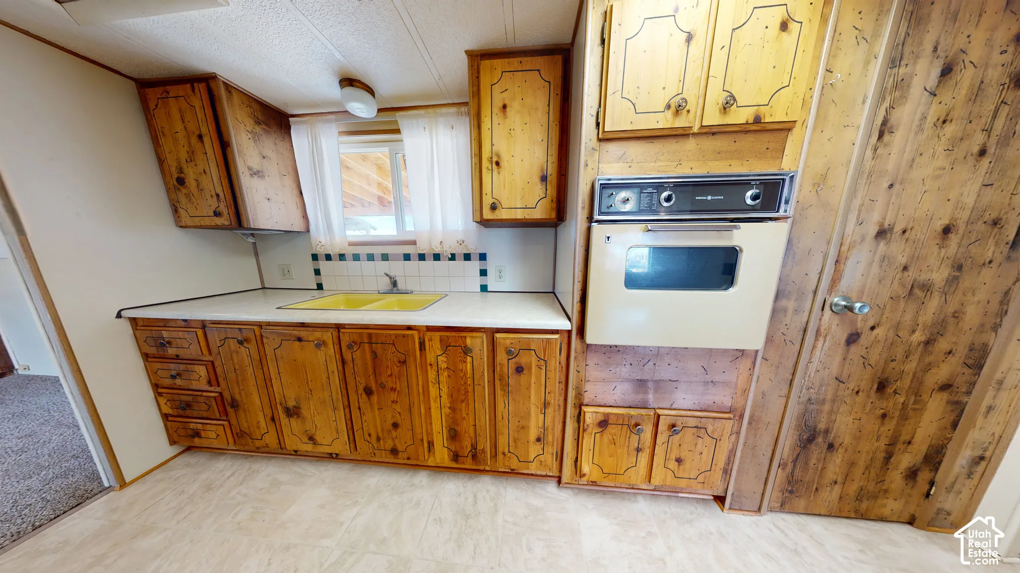 Kitchen featuring custom knotty wood cabinetry, built-in wall oven, dual-basin sink, and tiled backsplash