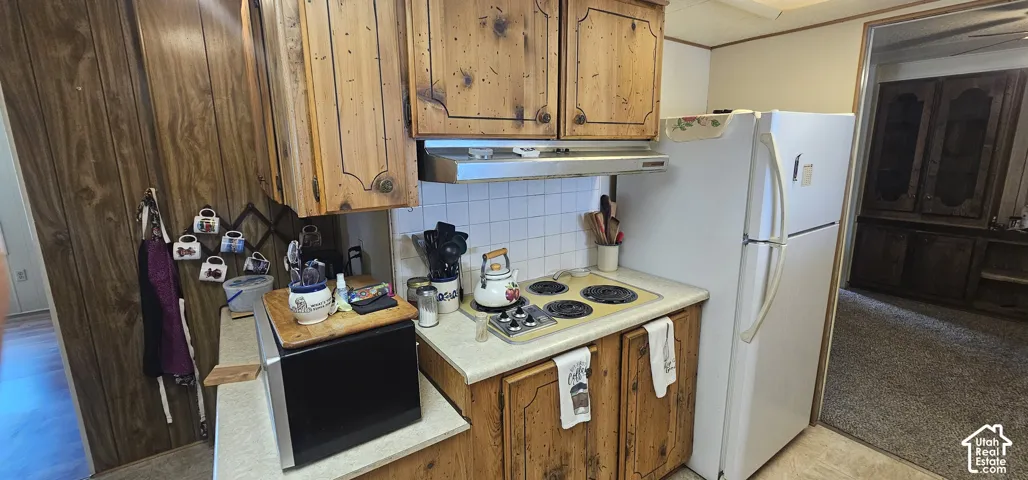 Kitchen featuring wood-finish cabinetry, white tile backsplash, and a built-in range hood