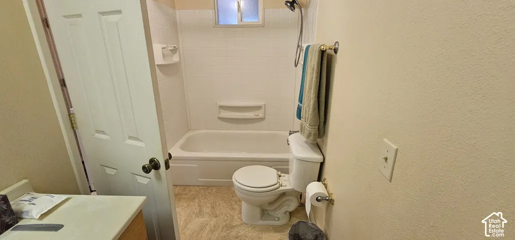 White bathtub with integrated shower, white tiled surround, and a small transom window