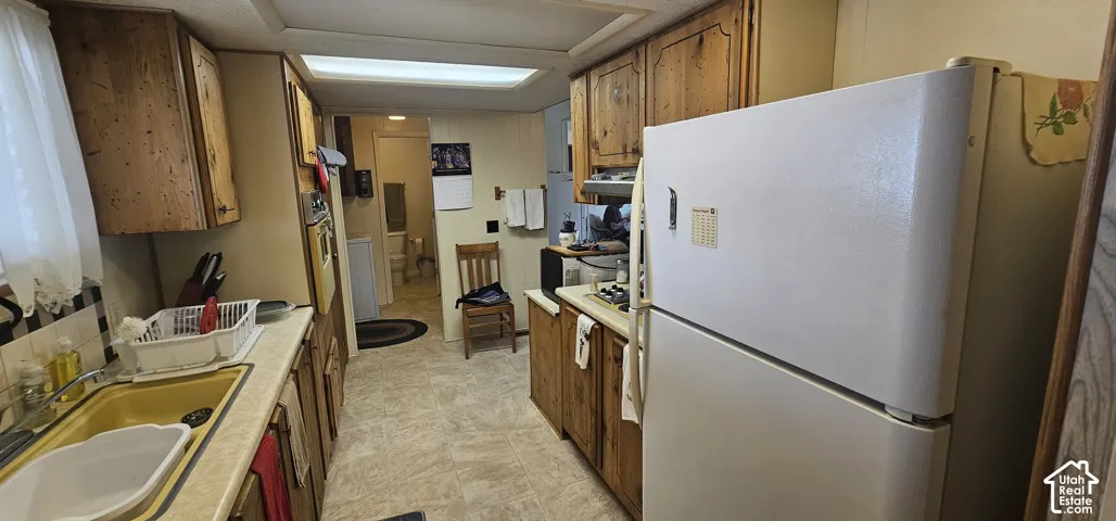 Kitchen featuring wood-finish cabinetry, a yellow dual-basin sink, and a white top-freezer refrigerator