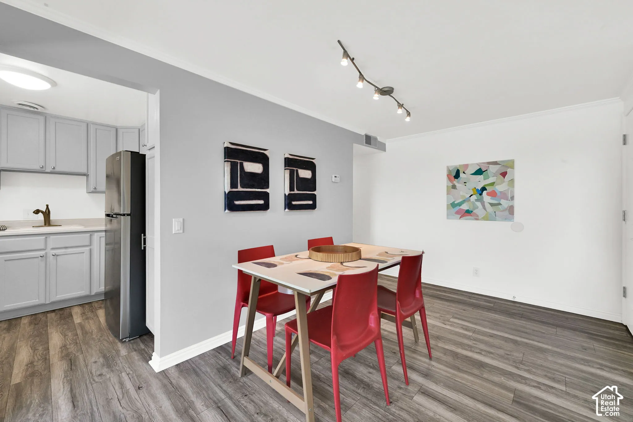 Wood-finish flooring throughout, track lighting, and a kitchen featuring light gray cabinetry, a stainless steel refrigerator, and a dark bronze finish faucet