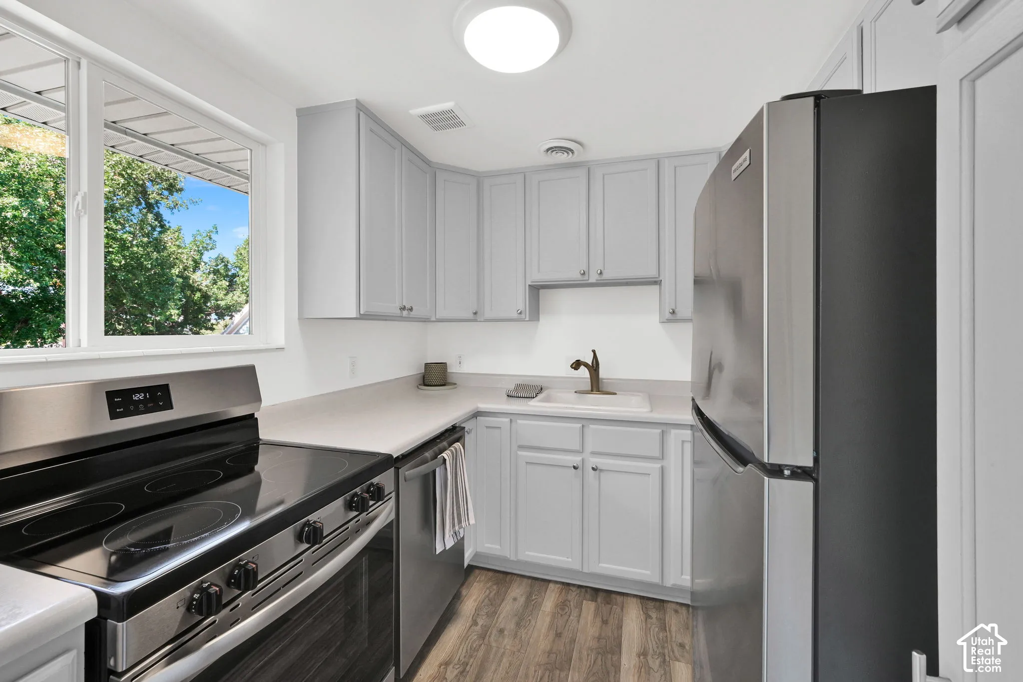 Kitchen featuring stainless steel appliances, light gray cabinetry, light countertops, wood-finish flooring, and a window