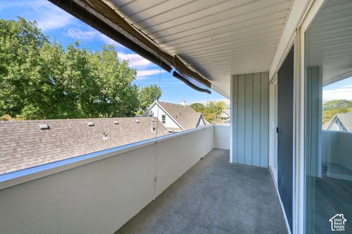 Outdoor balcony featuring a textured concrete surface, light-colored railing, and a sliding glass door
