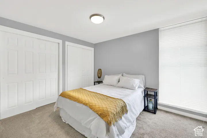 Neutral tone wall color, carpeted flooring, two sliding panel closet doors, ceiling-mounted light fixture, and window with blinds