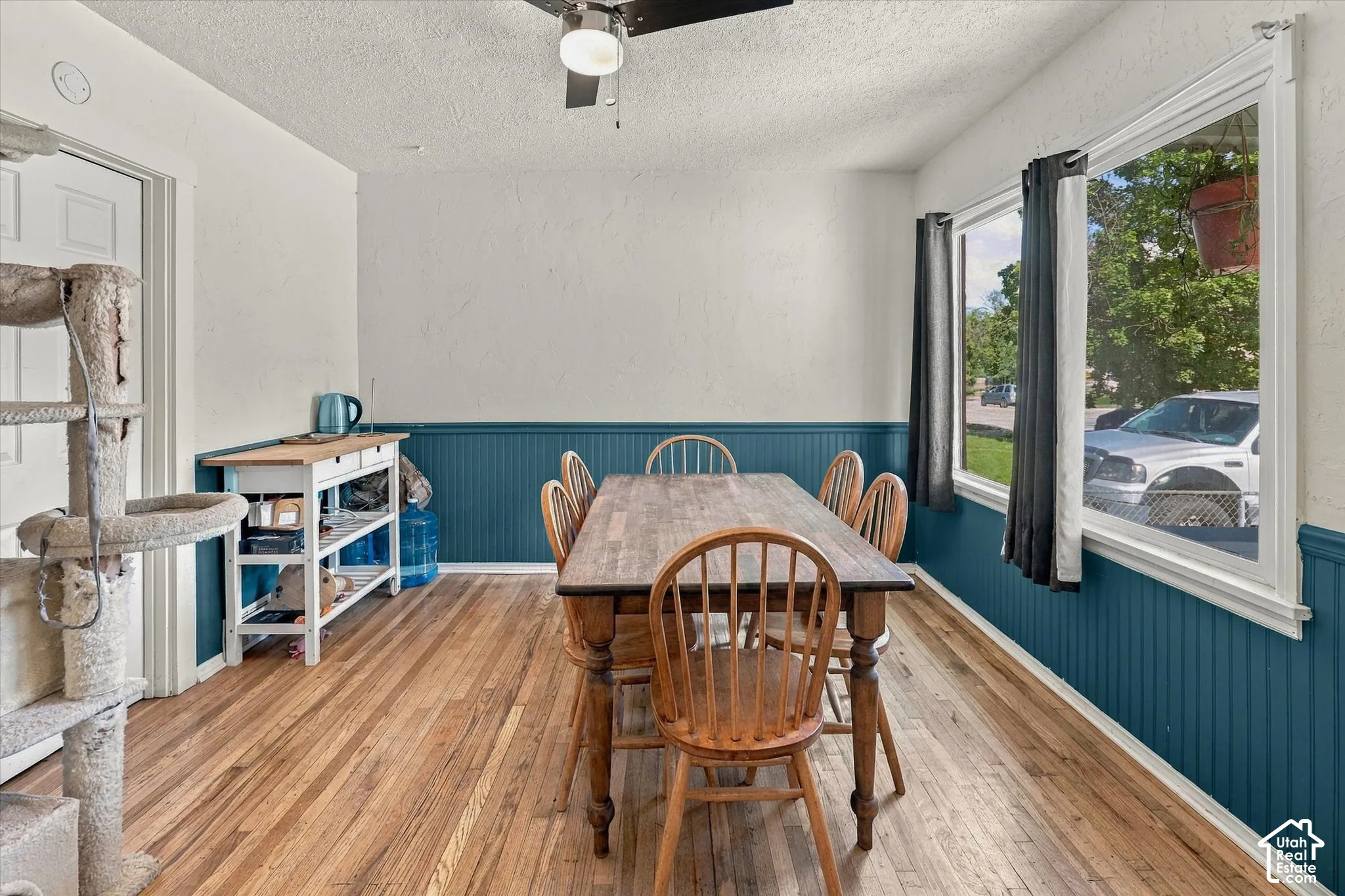 Hardwood flooring, painted wainscoting, ceiling fan with light fixture, white trim, and multiple windows