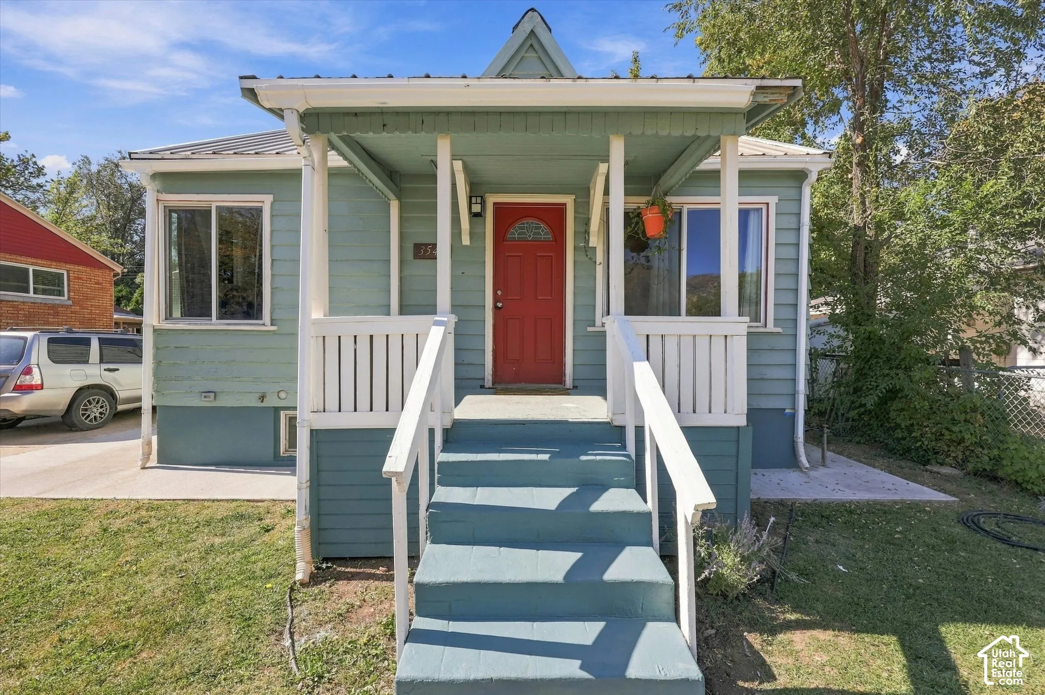 Front exterior featuring a covered porch, red entry door, white railings, and siding with horizontal panels
