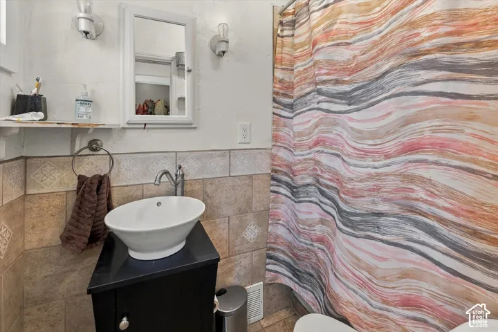 Wall-mounted medicine cabinet, wall-mounted light fixtures, vessel sink with chrome faucet, tiled wall surround, and corner vanity cabinet