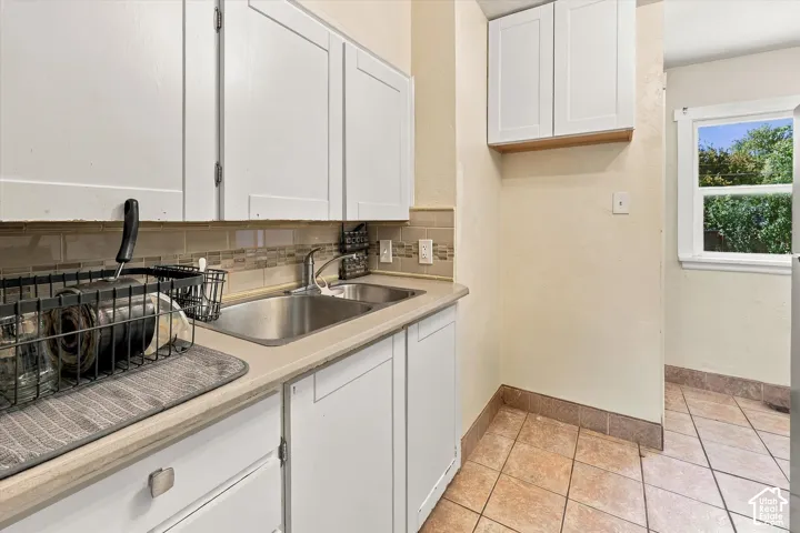 Kitchen featuring white upper and lower cabinetry, dual basin stainless steel sink, light-toned countertop, and tiled backsplash