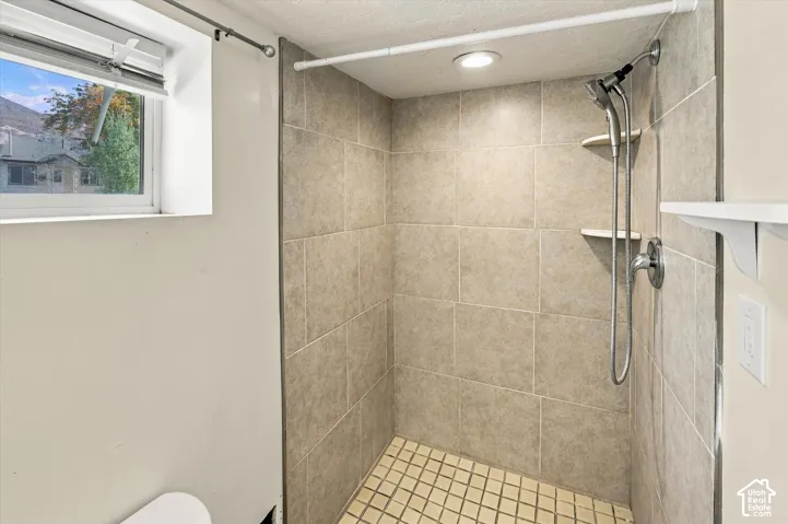 Tiled shower enclosure featuring a handheld showerhead, recessed lighting, and integrated shelving