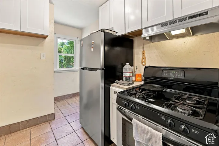 Kitchen featuring a gas range, stainless steel refrigerator, white upper cabinetry, and tile flooring