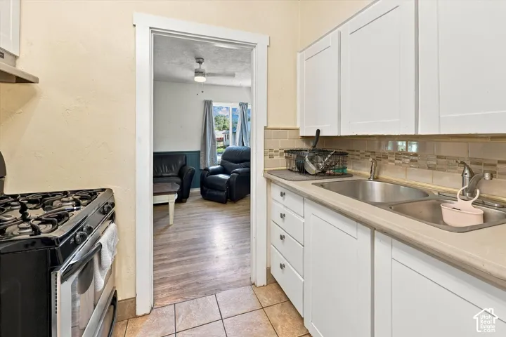 Kitchen featuring white cabinetry, dual basin stainless steel sink, and light-toned tile backsplash