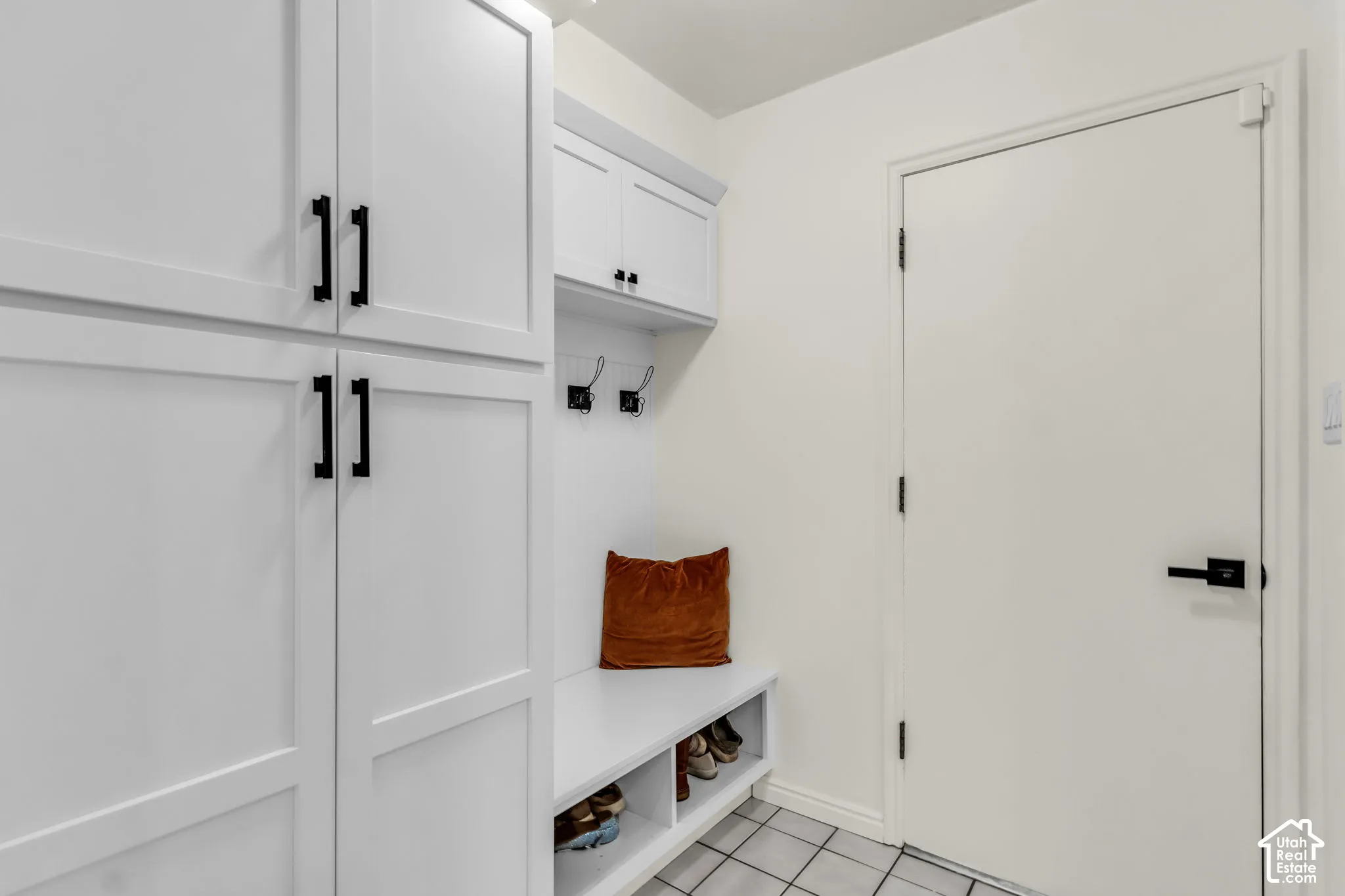 Built-in white cabinetry with matte black hardware, integrated bench seating, wall-mounted hooks, and tiled flooring
