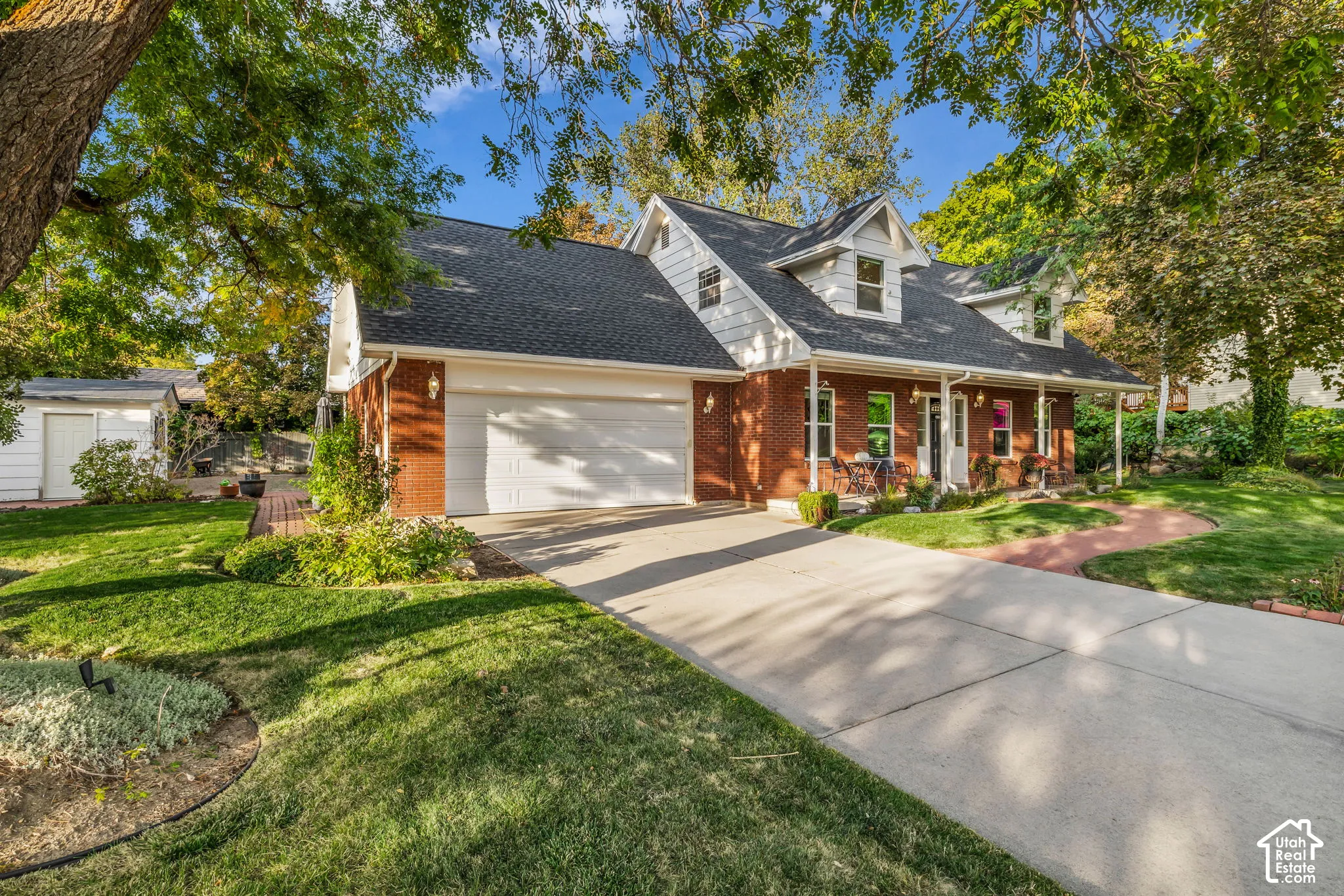 Brick facade residence featuring a covered front porch, dormer windows, and an attached two-car garage