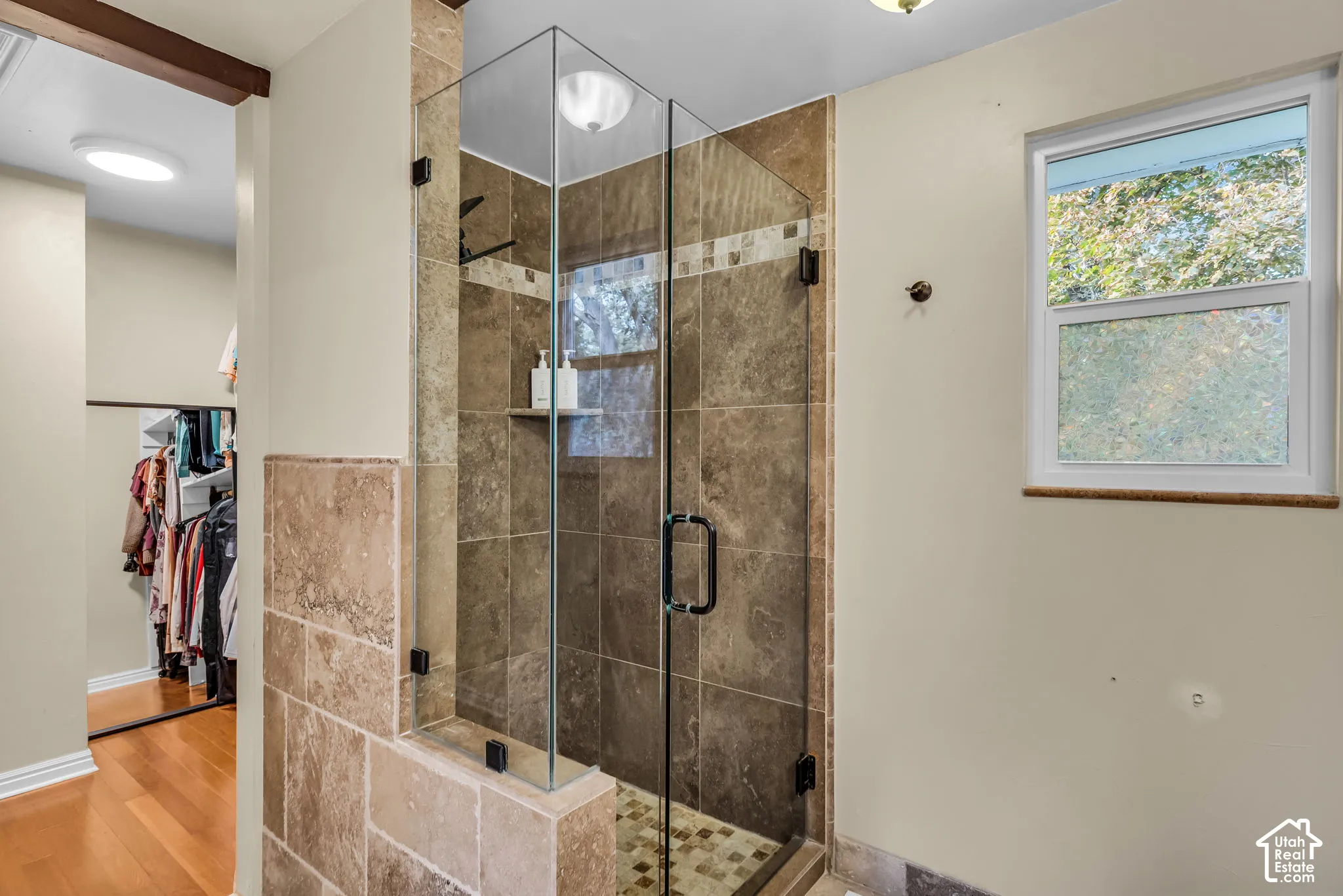 Glass-enclosed shower with stone tile surround, mosaic tile shower floor, and built-in shower shelf