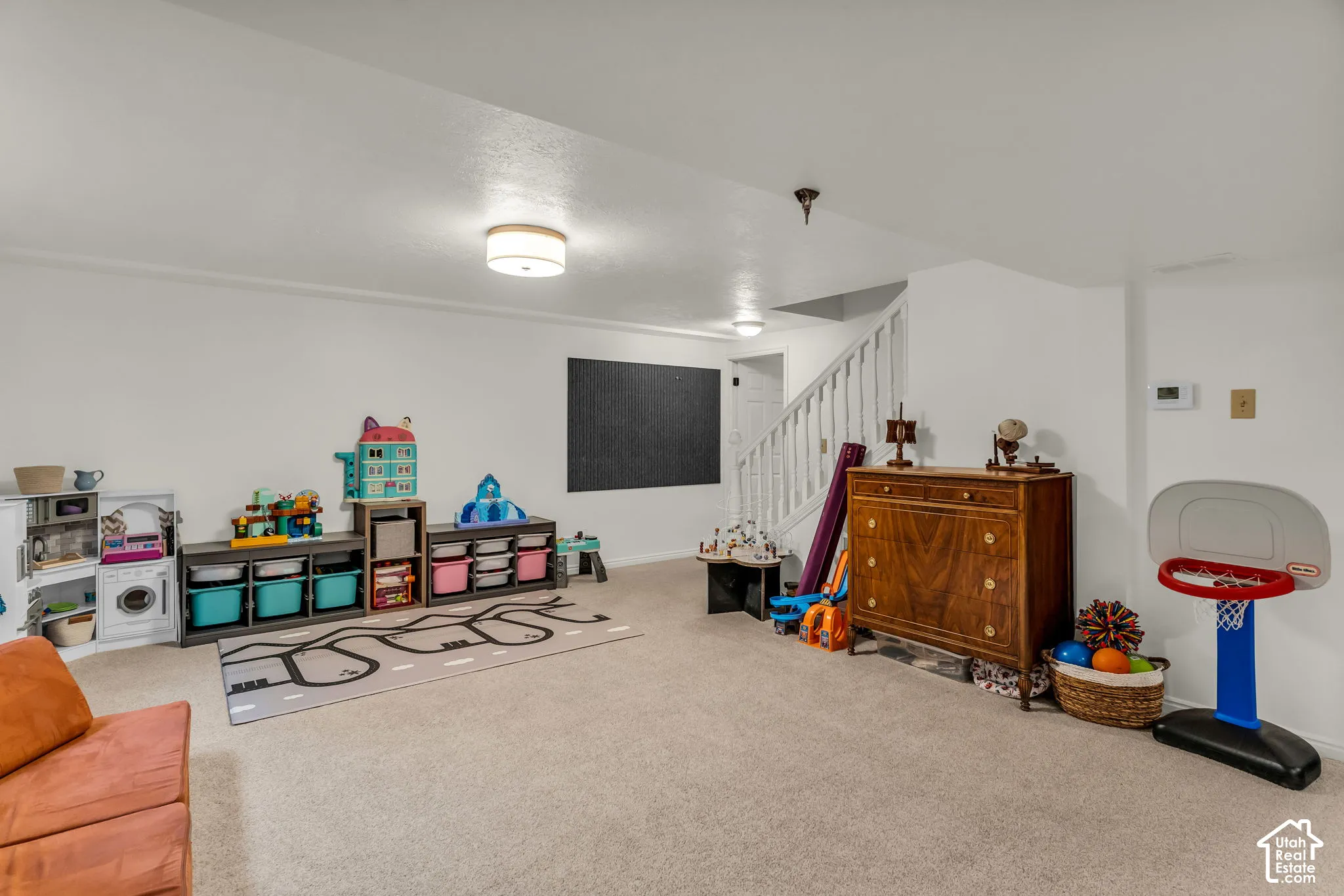 Expansive carpeted room featuring white walls, recessed ceiling lights, and a staircase with white railings