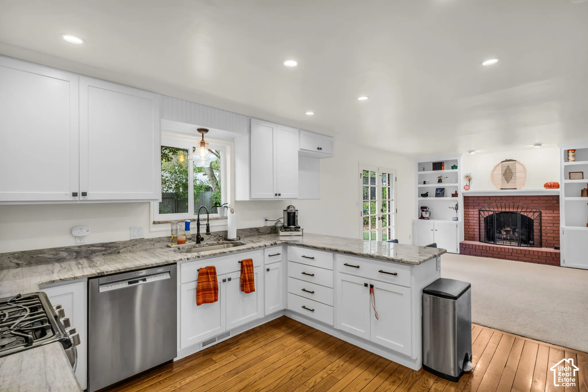 White cabinetry, stone countertops, stainless steel appliances, wood-finish flooring, and a brick fireplace