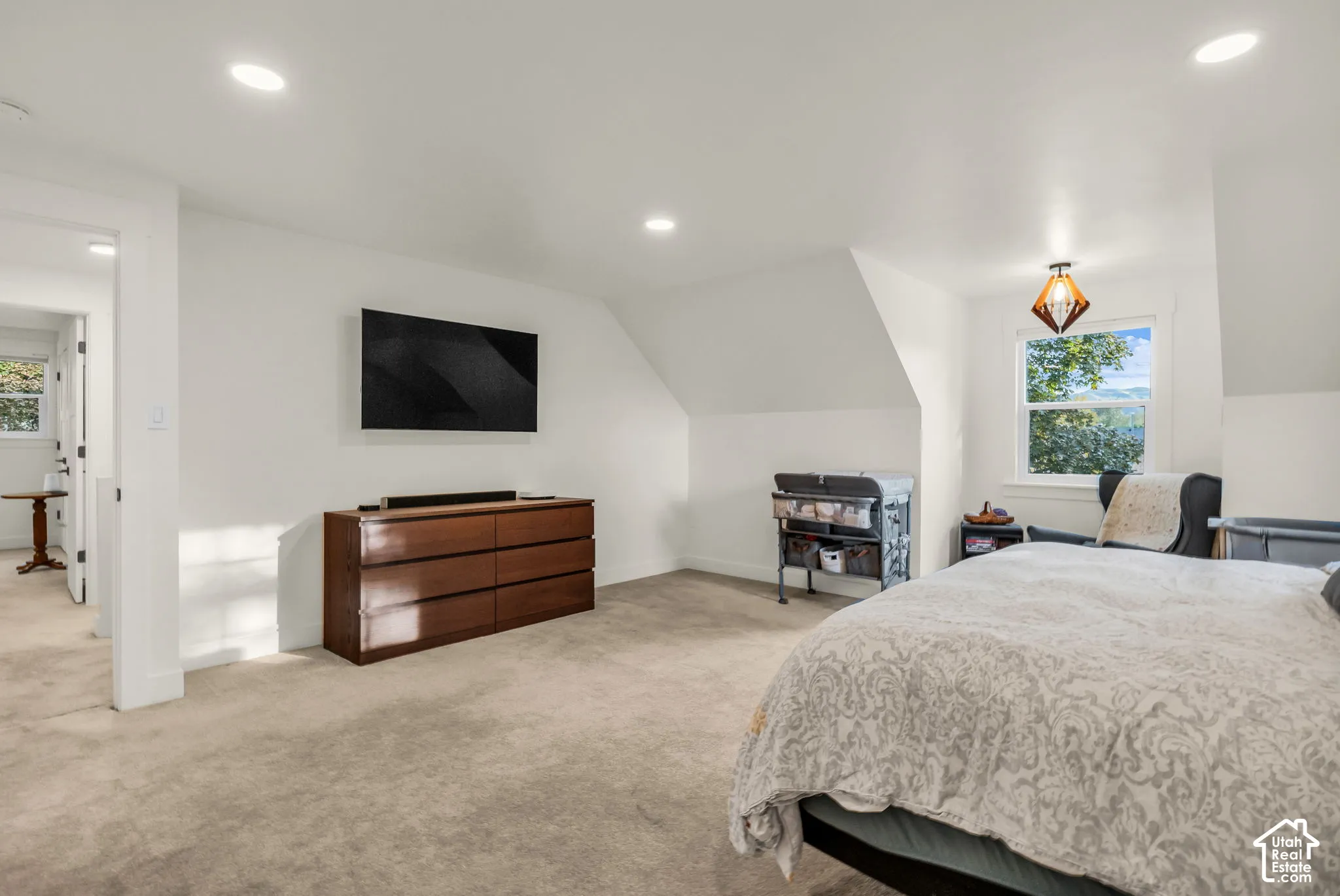 Recessed ceiling lighting, white walls, angled ceilings, window with exterior scenery, and a modern geometric pendant light fixture