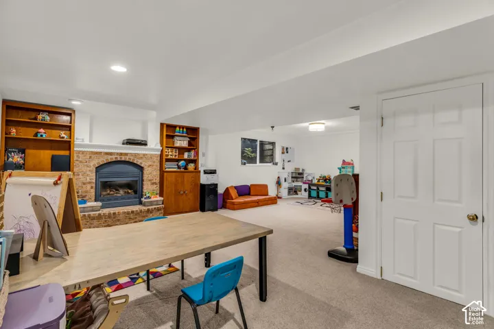 Spacious room featuring a brick-surround fireplace with a dark metal insert, built-in wood shelving, recessed lighting, and light-colored carpeting